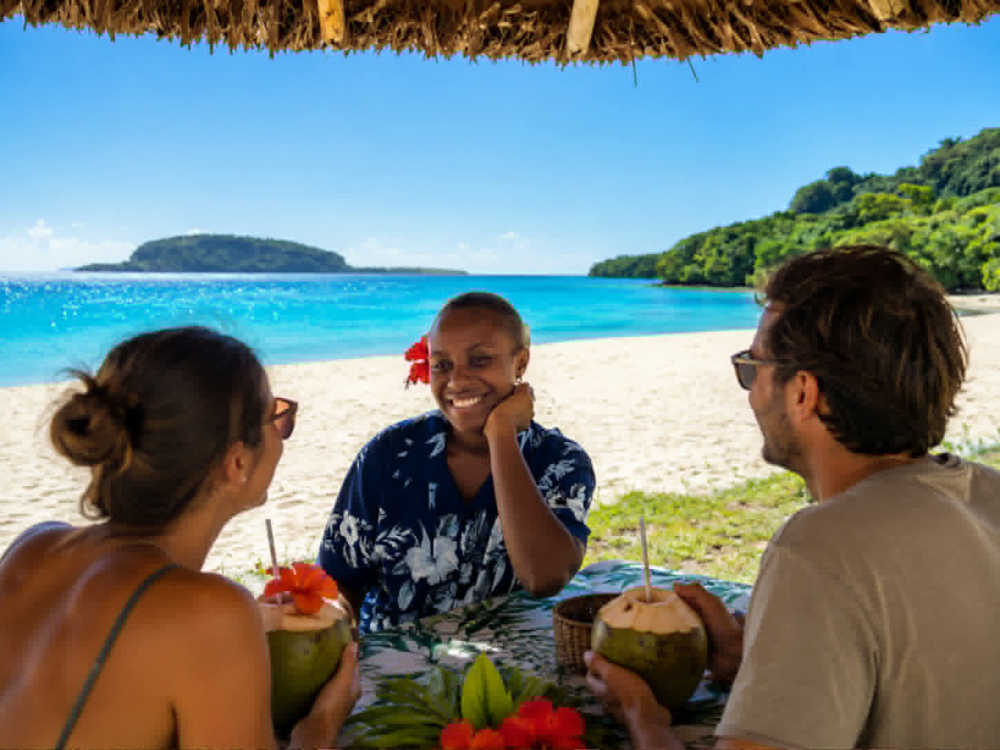 Guests and local team enjoying fresh coconuts beside the beach